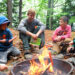 Campers and Counselor at Camp O-AT-KA in Sebago Maine cook hot dogs over a campfire.
